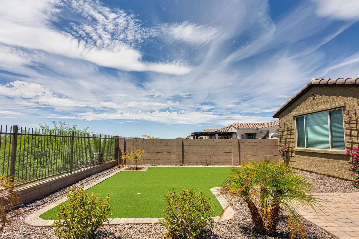 This exterior image features a manicured artificial grass area framed by palm trees and a bordering wall, all beneath a vast sky dotted with clouds. The space suggests opportunities for outdoor relaxation, family gatherings, and enjoying natural beauty, with the ambiance shifting between lively and tranquil depending on the season.
