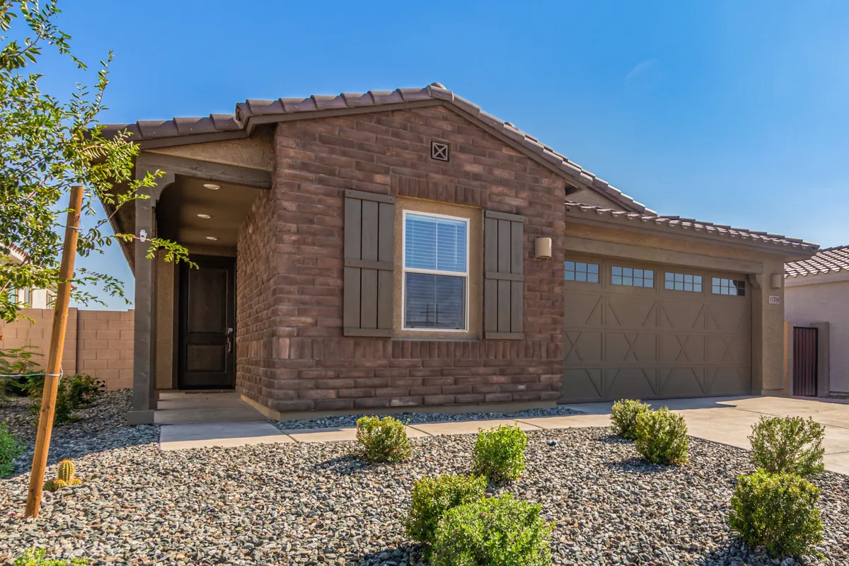 An inviting view of the home's exterior, showing the stone facade, prominent front door, and the spacious two-car garage. The setting feels welcoming, with well-maintained landscaping hinting at a friendly residential community.