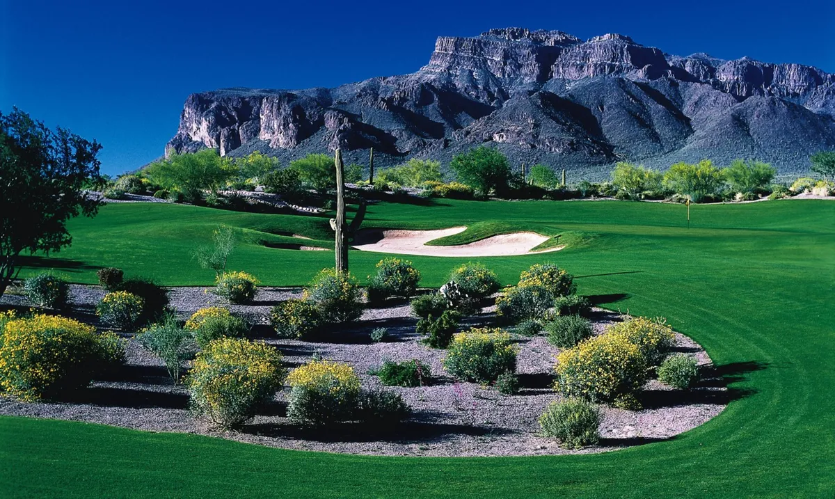 A lush green golf course set against a backdrop of desert flora and majestic mountains. The scene exudes tranquility and provides a sense of Arizona’s unique outdoor lifestyle, with hints of neighborhood activity and local flavor.