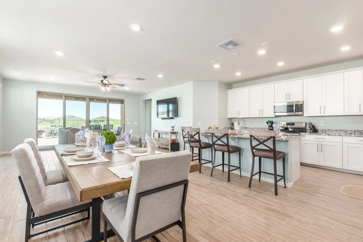 This image showcases an open-concept living space that seamlessly blends the dining table, kitchen island, and living area. Large windows flood the space with natural light, and there's a clear view of a TV positioned for optimal movie nights. The inviting furnishings and integration of the three main gathering areas highlight the home's welcoming and communal atmosphere.
