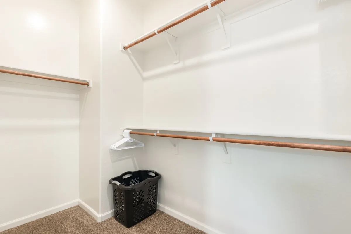 A clean, functional closet area with hanging rods, an empty space for storage, and a laundry basket. The minimalist design emphasizes organization and ample storage for extended stays.