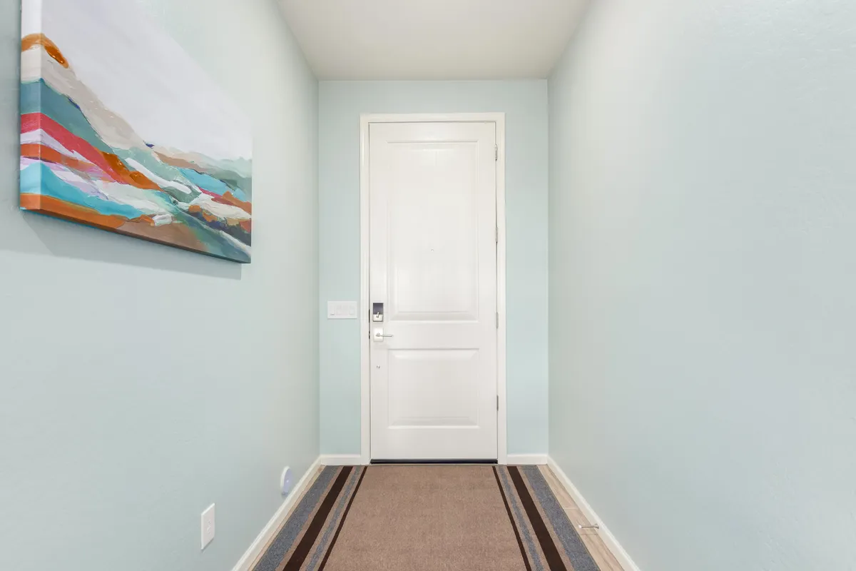 An inviting view of the home's entryway, highlighting a warmly lit area rug, tasteful artwork on the wall, and the front door. The space sets a welcoming tone and hints at the comfort awaiting just inside, echoing the transition from the outside world into a cozy, community-oriented home environment.