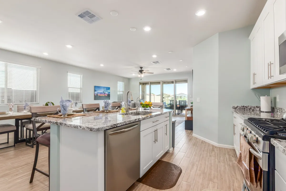 This image presents a modern kitchen with a prominent island, stainless steel appliances, and a view into the dining area. Large windows enhance the feeling of openness and light, while the spacious layout encourages social interaction—ideal for cooking, sharing meals, and entertaining guests.