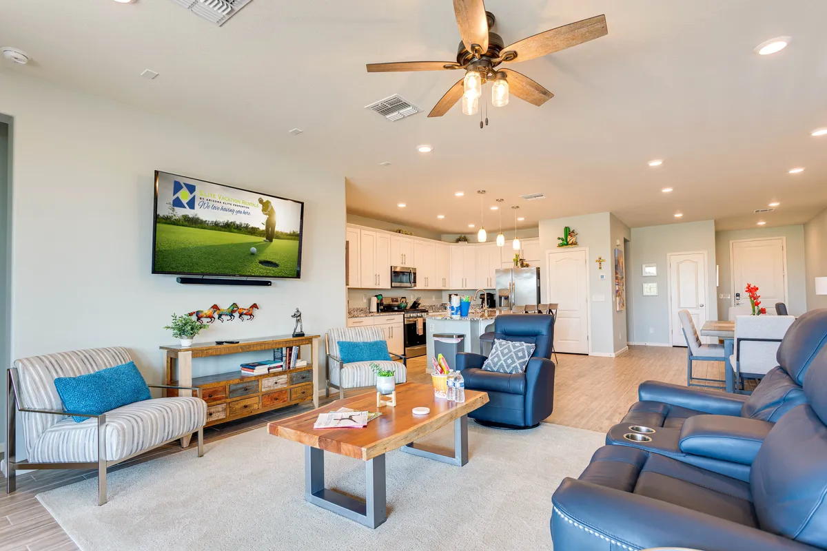 The scene shows a comfortable living area with a television displaying a golf scene, a coffee table, plush seating, and open visibility to the kitchen. The arrangement supports movie nights, socializing, and enjoying group activities indoors.