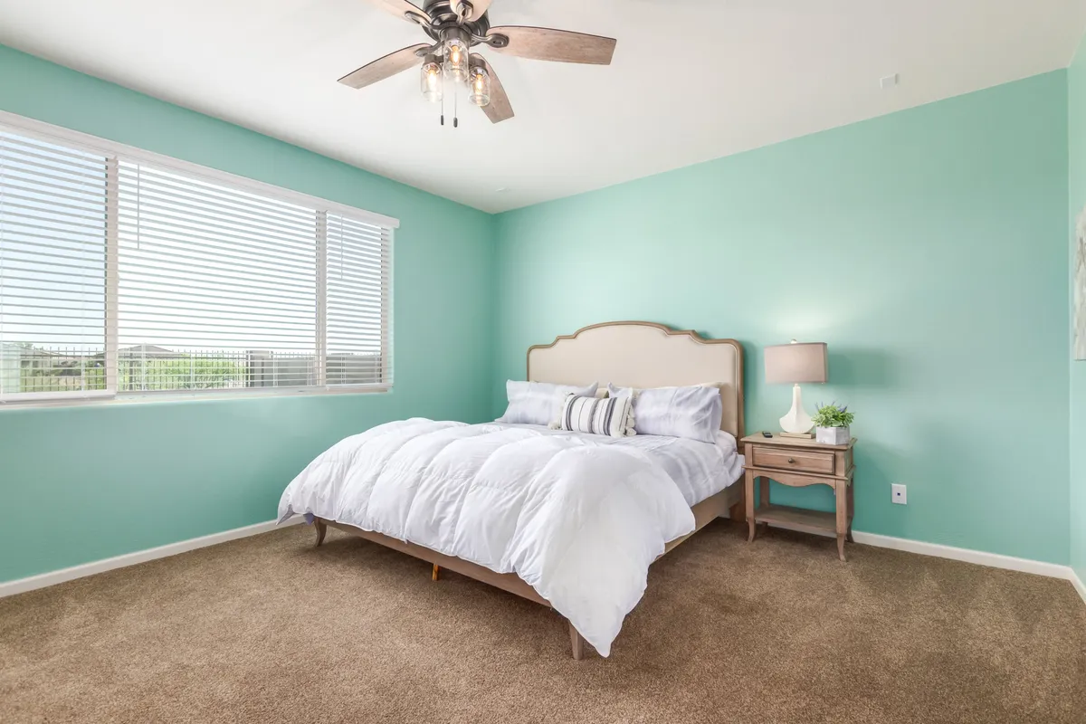 A tranquil bedroom featuring a bed with crisp white bedding, turquoise walls creating a soothing environment, and a nightstand with a lamp. Soft natural light streams in through a window, highlighting the restful, refreshing vibe of the space.