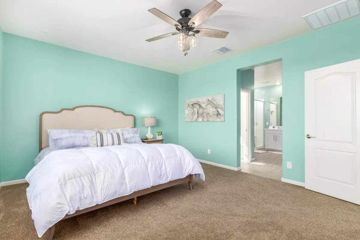 A cozy bedroom with a bed dressed in white linens, a turquoise accent wall, ceiling fan with light, and a nightstand with a lamp. The space feels peaceful and inviting, perfect for relaxation and sleep.