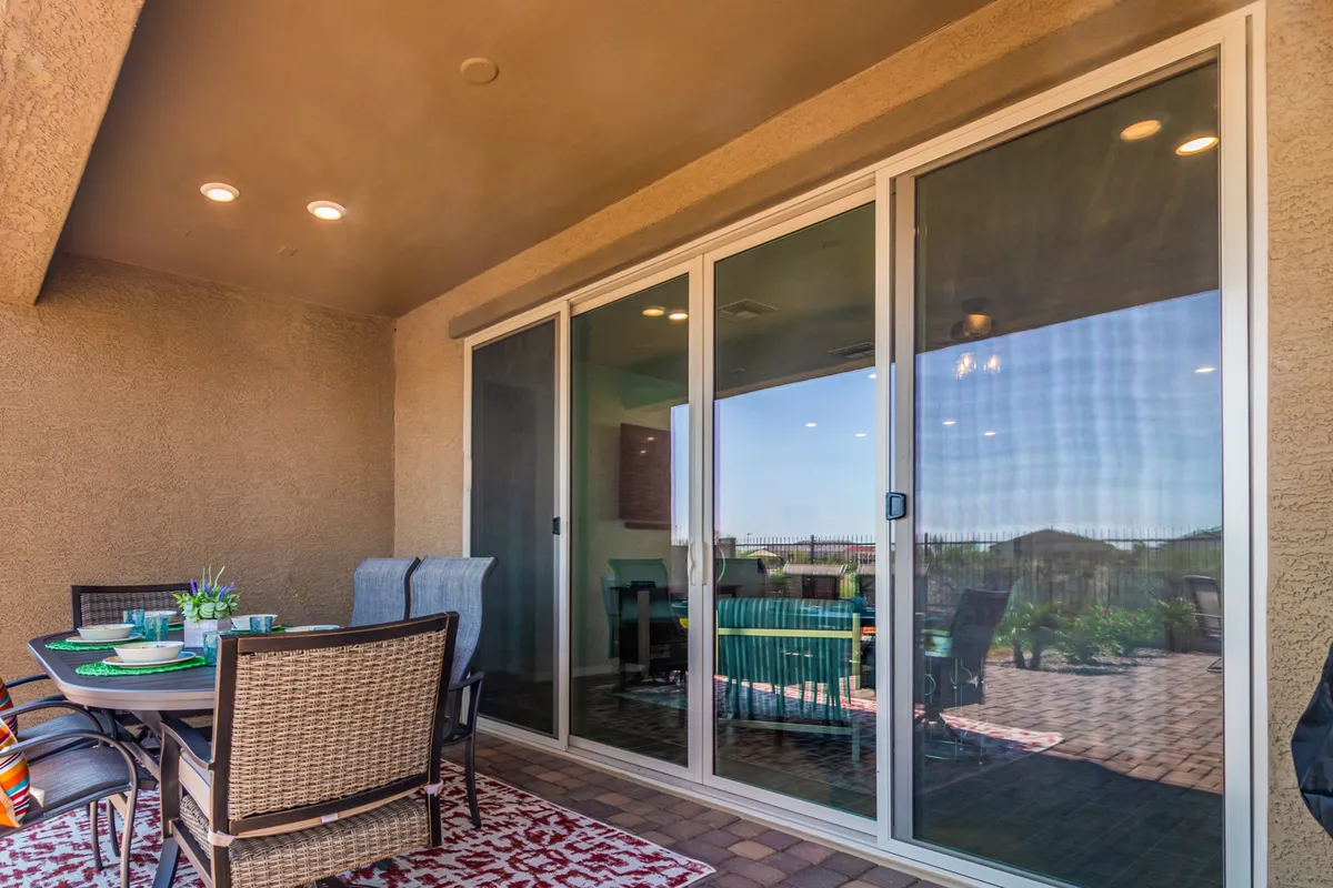 A stylish outdoor dining area directly connected to the interior via wide sliding glass doors. The setup features a modern dining table with six chairs on a decorative rug, seamlessly blending indoor comforts with the fresh air and natural light of the patio.